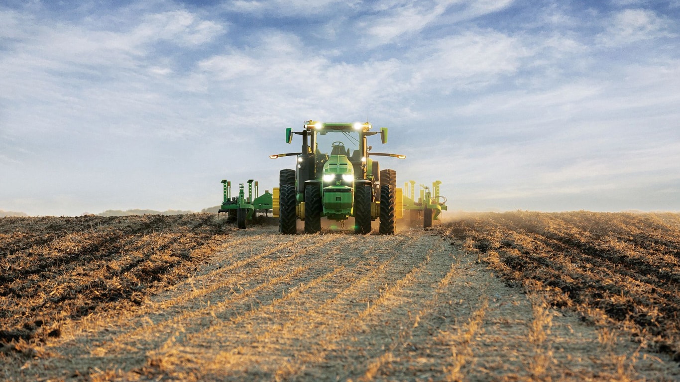 Önjáró John Deere traktor, amely a talajművelő eszközt nyílt terepen vontatja.