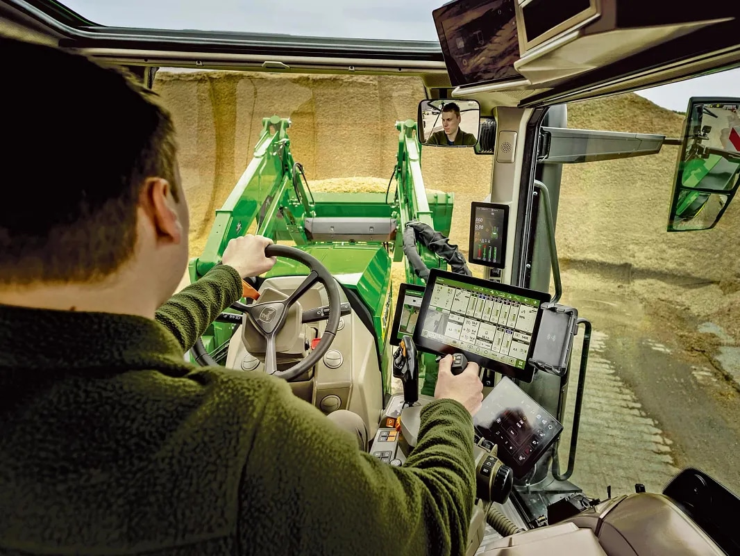 A John Deere traktor belső fülkéjéből a kezelőszervek és a homlokrakodó működése látható.