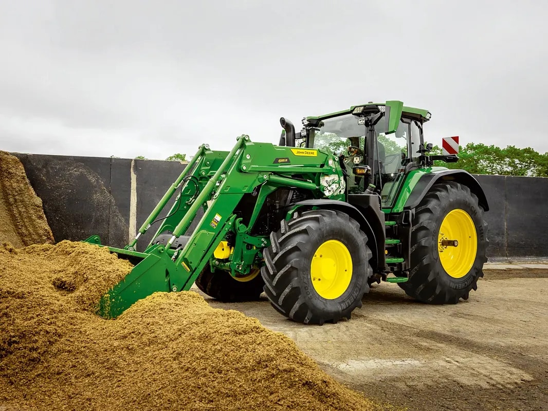 A John Deere traktor egy silóhalomba tolódik a homlokrakodó kanállal a gazdaság környezetében.