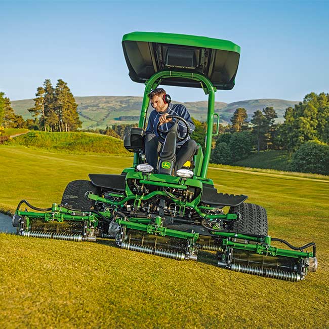 Egy golfpálya-karbantartó a golfpályán dolgozik, John Deere zöld fűnyírót vezet elölnézetből.