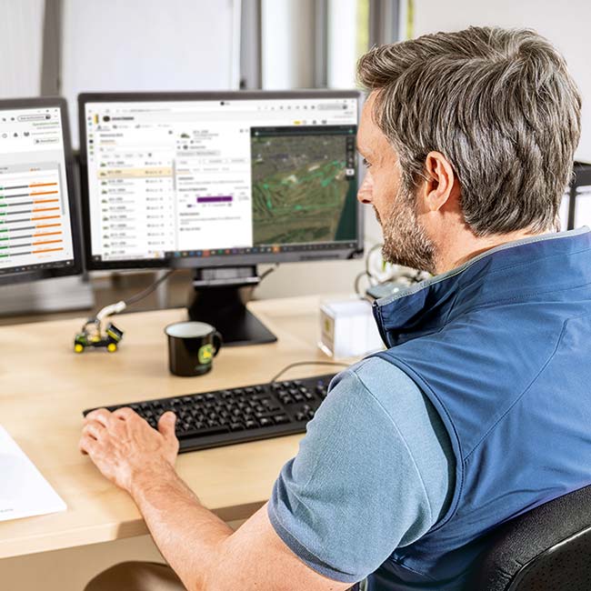 Vezető golfpálya-gondozó ül az irodájában, és áttekinti az intelligens golfpálya-gondozási technológia által gyűjtött adatokat.