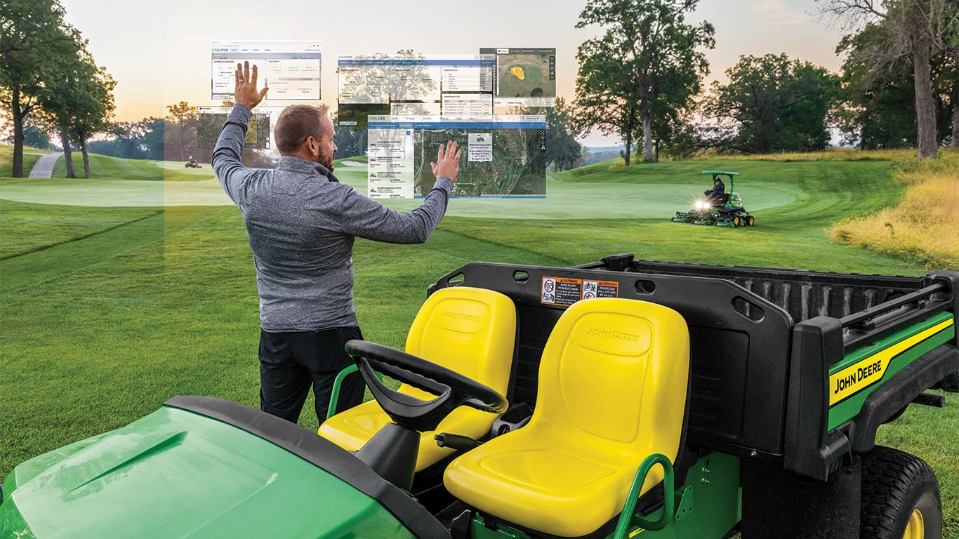 Egy golfpálya-karbantartó üzemelteti a képzeletbeli Smart Green Keeping kijelzőket a levegőben egy golfpályán.