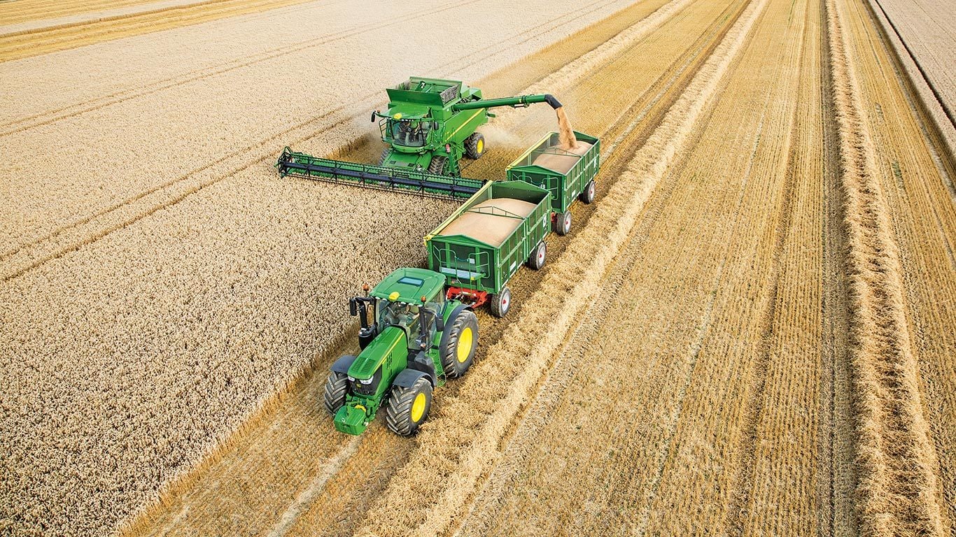 John Deere S sorozatú kombájn búzát ürít traktorral vontatott kettős pótkocsikba.