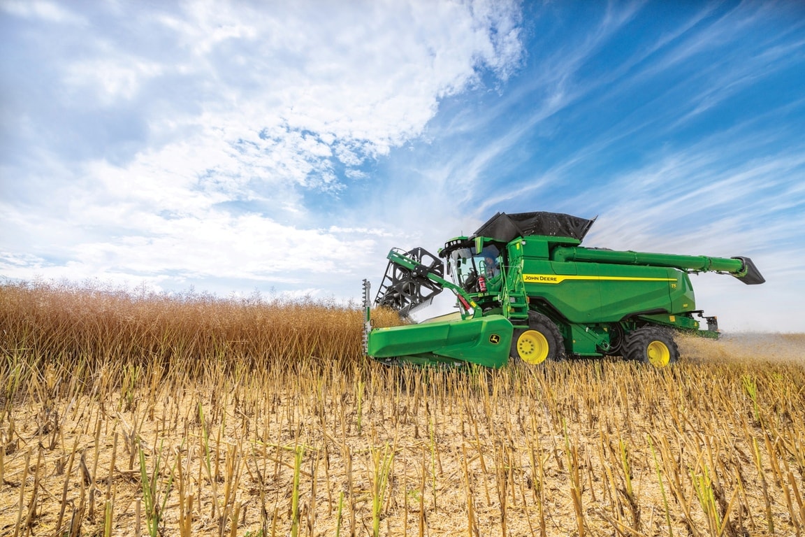 A John Deere kombájn gabonát takarít be úgy, hogy a vágóasztal a szántóföldön, a kék ég alatt legyen a betakarítás során