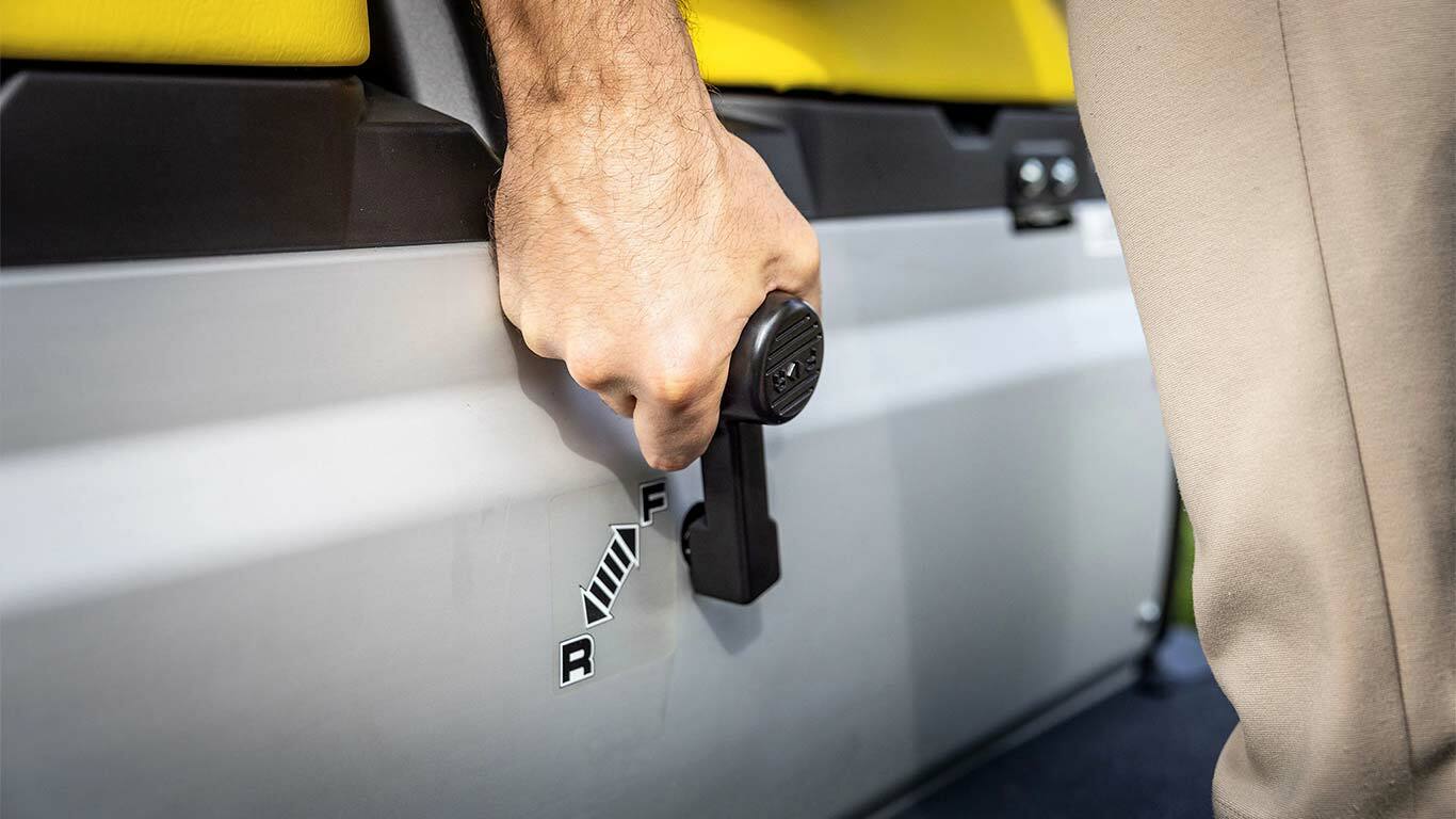 A sebességváltó kart a John Deere Gator GS-en működtető kéz közelképe, amely a sárga ülések mellett előremeneti és hátrameneti pozíciókat mutat.