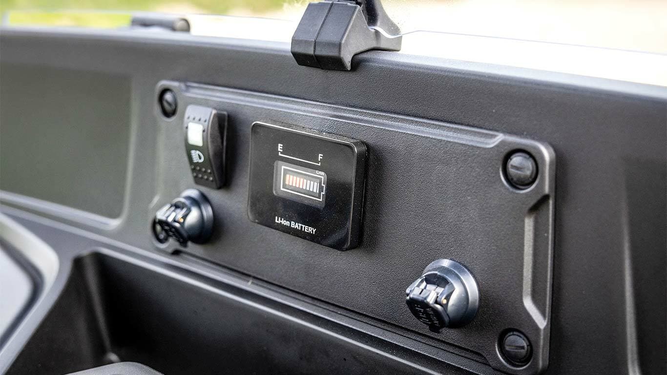 Egy John Deere Gator GS elektromos modell műszerfala, amely az akkumulátor töltöttségi szintjelzőt és a tápfeszültség csatlakozókat mutatja.