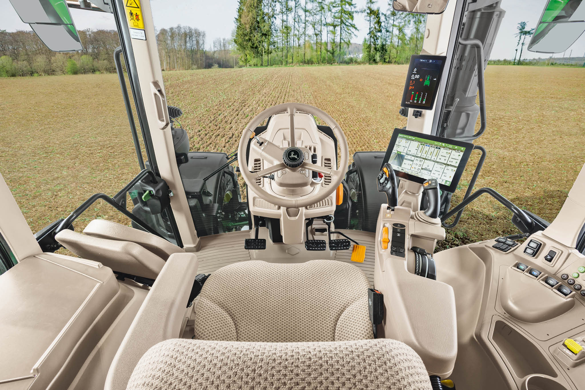 John Deere 6M sorozatú traktor vezetőüléssel, kormánykerékkel és digitális kijelzőkkel ellátott fülkéjének belső áttekintése.