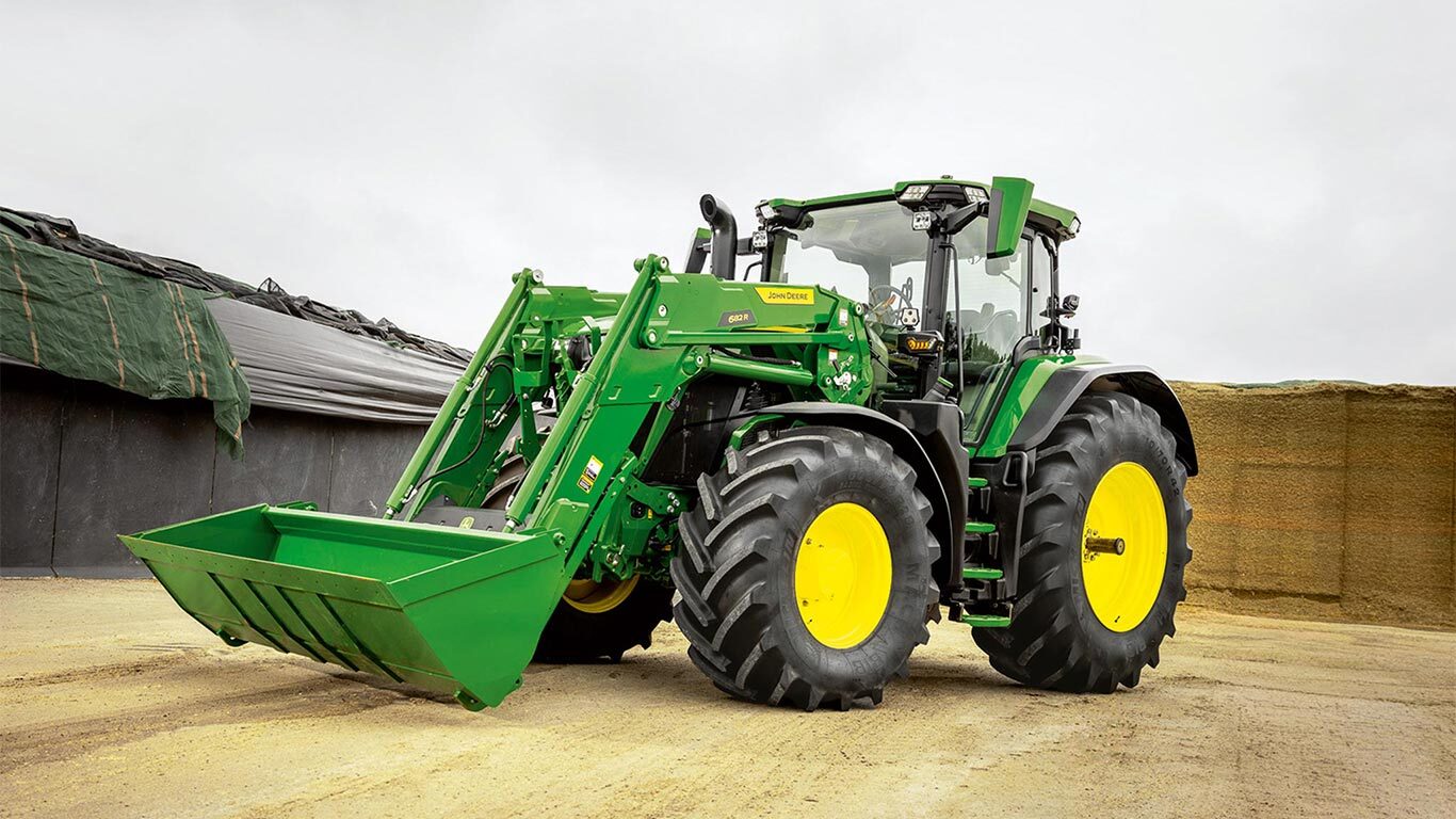 John Deere traktor homlokrakodóval, amely a silótároló közelében, egy gazdaság területén áll.