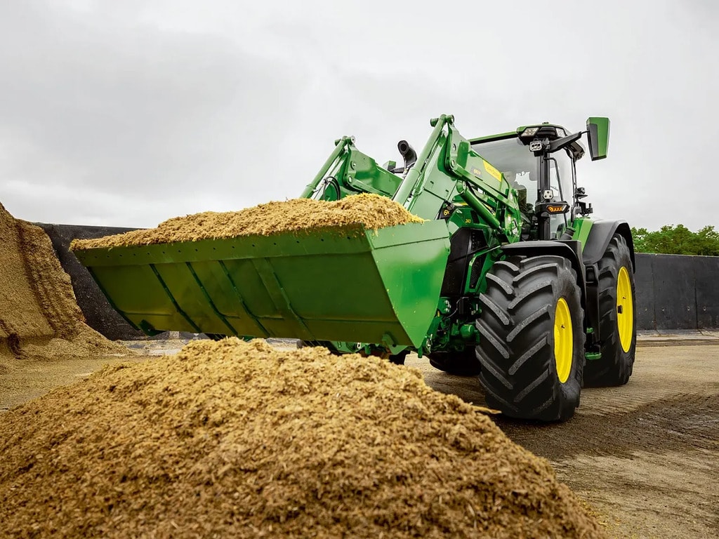 A John Deere traktor homlokrakodóval szállítja a szecskázott silótakarmányt egy mezőgazdasági tárolóhelyen.