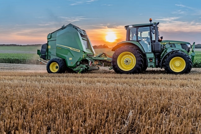 Egy John Deere 6M 150 által vontatott John Deere V462M egy szalmás tarlón napnyugtakor