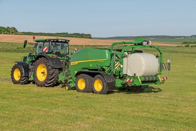 Egy John Deere 6R 185 által vontatott John Deere C442R csomagoló bálázó nagy tömörségű silótakarmány bála készítése során
