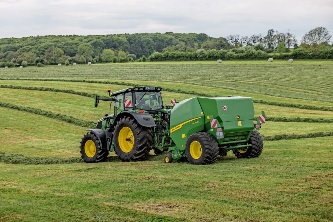 Egy John Deere 6M traktor által vontatott John Deere F442R bálázó egy dombos füves területen