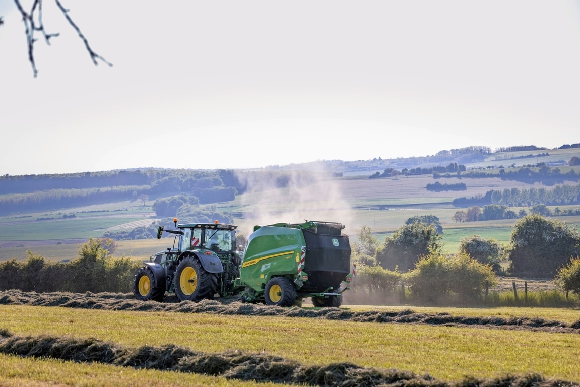 Egy John Deere 6R 185 traktor által vontatott John Deere V462R széna bálázás során