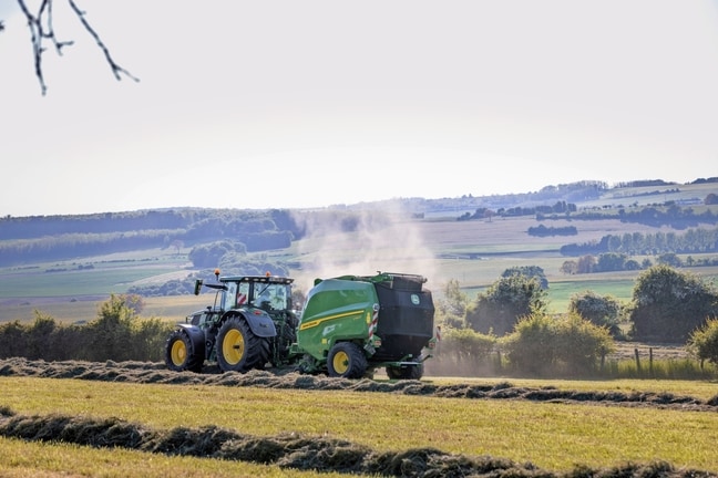 Egy John Deere 6R 185 traktor által vontatott John Deere V462R széna bálázás során